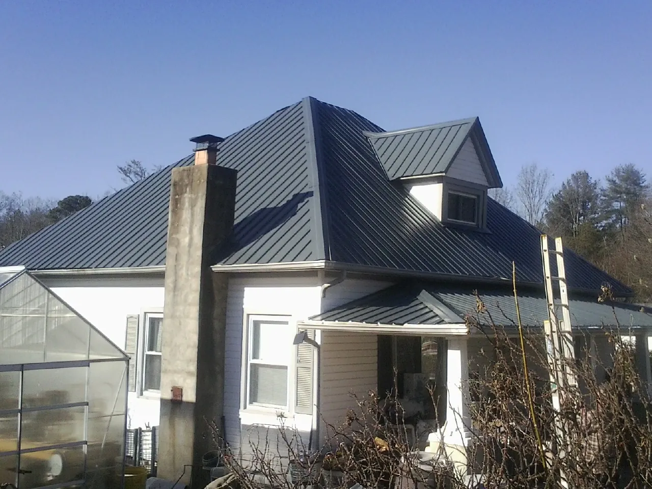 Dark blue standing seam metal roof on a white farmhouse with dormer — Slate & Tile Roof Repair by Roofing Brothers in Mont Belvieu