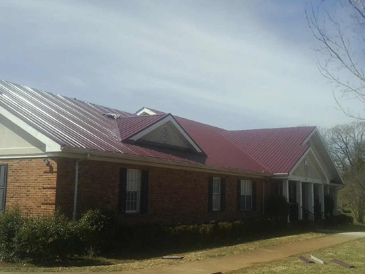 Red metal roof with gabled entries on a long brick building, from a Hail Damage Roof Repair job in Mont Belvieu