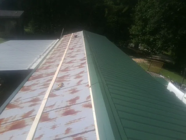Old rusted panels beside newly installed green metal roofing — Wind Damage Roof Repair by Roofing Brothers in Mont Belvieu