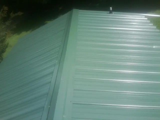 New green metal panels meeting at the ridge of a roof — Flat Roof Repair work by our crew in Mont Belvieu