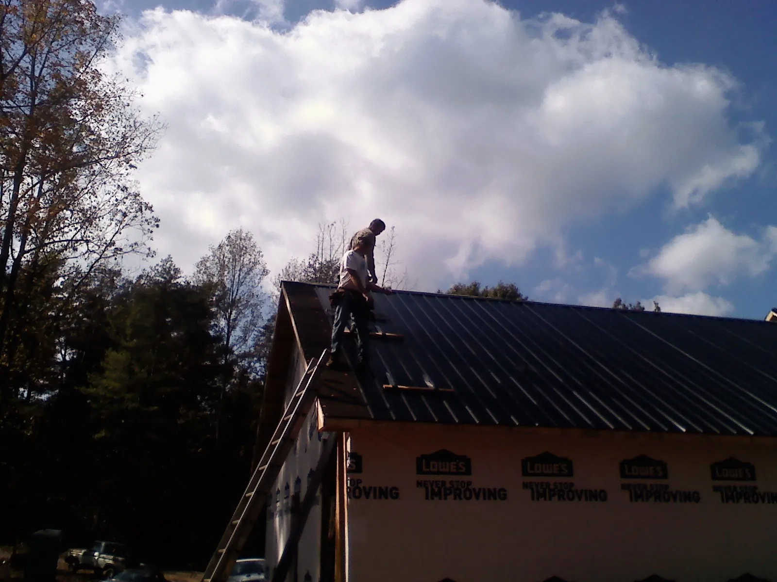Roofer fastening dark metal panels high against a cloudy sky, from a Roof Inspection job in Mont Belvieu