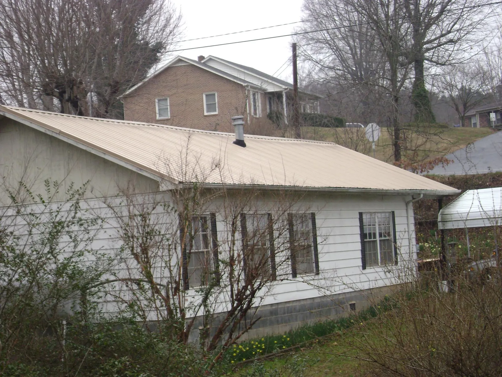 Tan metal roof on a white sided house set into a hillside — Commercial Roofing by Roofing Brothers in Mont Belvieu