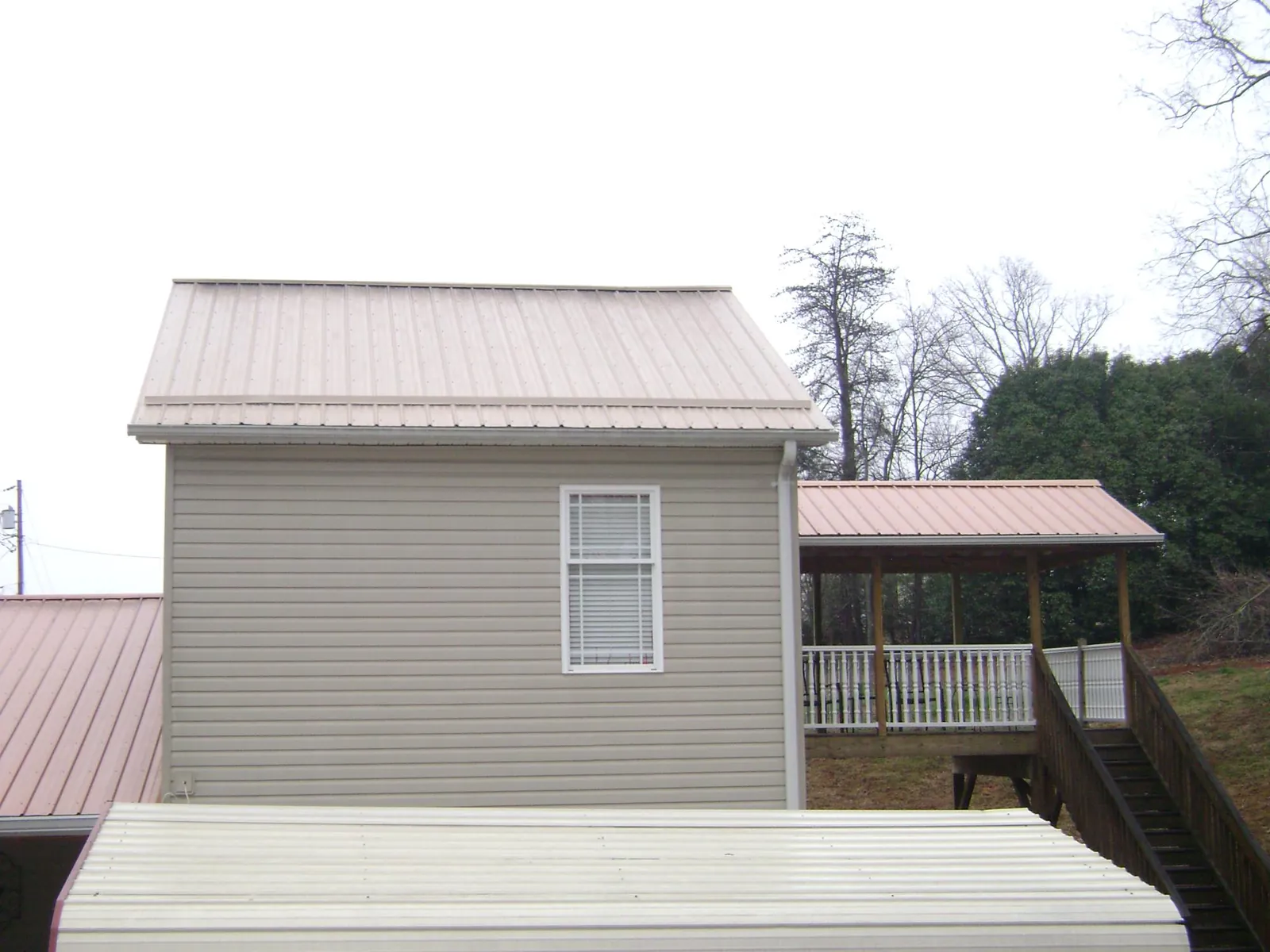 Tan metal roofs on a two story addition and attached porch, from a Roof Replacement job in Mont Belvieu
